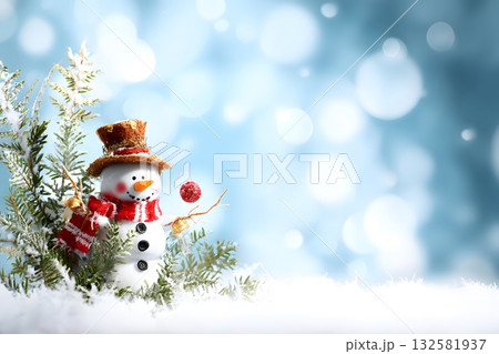 A cheerful snowman dressed for winter stands among snowy pine branches holding a festive Christmas ornament. 132581937
