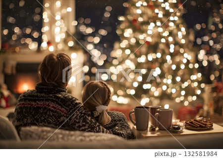 Couple enjoys a cozy Christmas evening with warm drinks by the fire and tree. 132581984