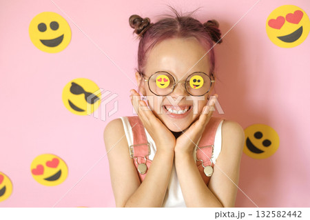 A laughing, cheerful girl with glasses and a variety of emoji icons. 132582442
