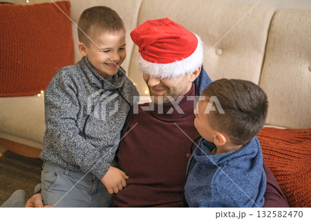 A father in a red Santa Claus hat plays with children. 132582470