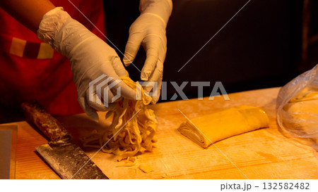 Hands making fresh handmade noodles on wooden table Hands making fresh handmade noodles on wooden table 132582482