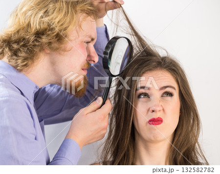 Man looking at woman hair through magnifer Man looking at woman hair through magnifer 132582782