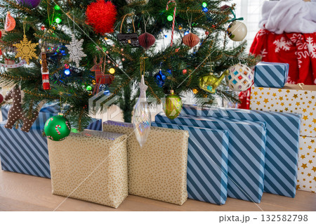 Wrapped gifts under decorated Christmas tree with glowing ornaments and festive lights at home Wrapped gifts under decorated Christmas tree with glowing ornaments and festive lights at home 132582798