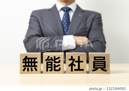「無能社員」と書かれたブロックと腕組みをするビジネスマン 132584092