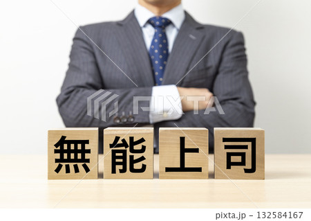 「無能上司」と書かれたブロックと腕組みをするビジネスマン 132584167