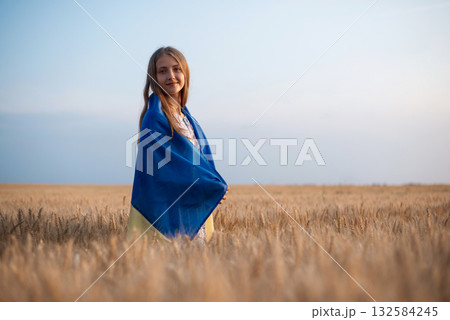 Smiling girl wrapped in ukrainian flag in the boundless field of rye at sunset. Patriotic ukrainian girl Smiling girl wrapped in ukrainian flag in the boundless field of rye at sunset. Patriotic ukrainian girl 132584245