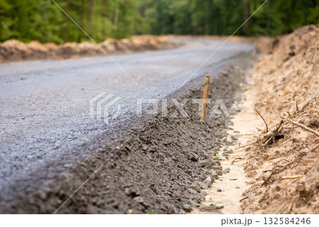 Close-up photo of new asphalt road pavement in the countryside. Constructing new high-quality road in the woods 132584246