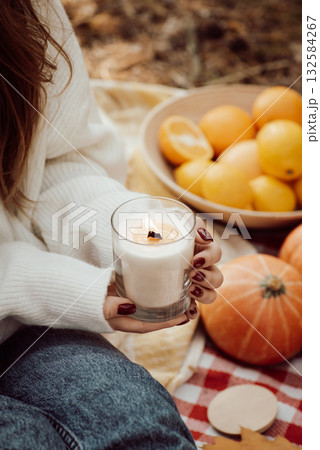 Girl holding aroma candle sitting on plaid. Picnic in Autumn park Girl holding aroma candle sitting on plaid. Picnic in Autumn park 132584267
