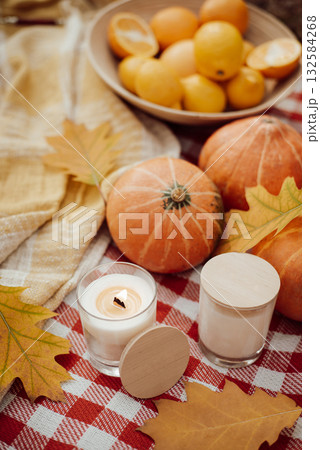 Bright photo of small pumpkins, oranges, burning aroma candles, warm plaid in Autumn colors with many bright oak leaves around 132584268