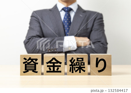 「資金繰り」と書かれたブロックと腕組みをするビジネスマン 132584417