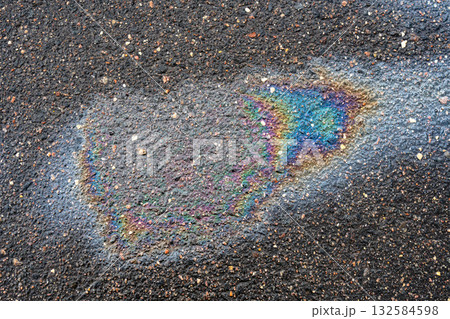 Oil spill on wet asphalt pavement showing multicolored rainbow sheen and pollution concept 132584598
