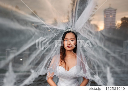 Chinese bride wearing wedding dress and veil by fountain Chinese bride wearing wedding dress and veil by fountain 132585040