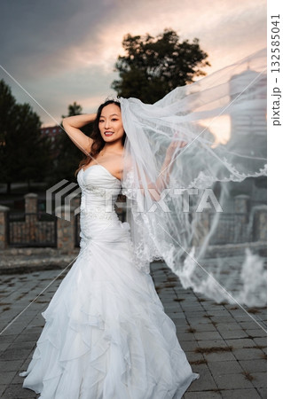 Chinese bride smiling in flowing wedding dress and veil at sunset Chinese bride smiling in flowing wedding dress and veil at sunset 132585041