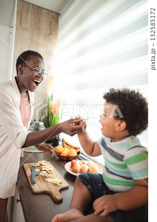 Mother feeding child banana in kitchen for healthy snack 132585172