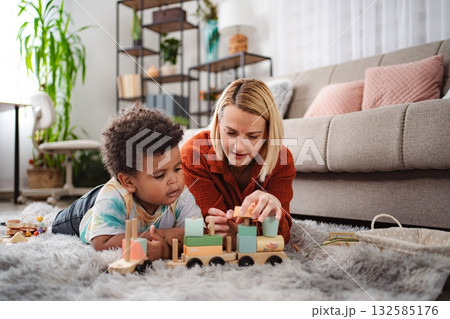 Mother and son playing with wooden toy train on living room floor 132585176