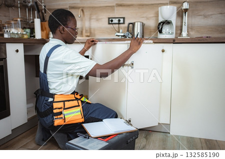 Handyman taking measurements of kitchen cabinets using tape measure 132585190