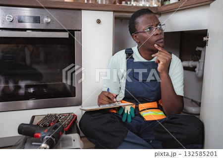 Plumber inspecting pipes and taking notes in kitchen 132585201