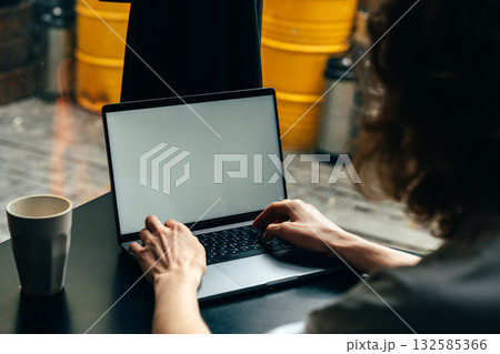 Working on a laptop at a cafe with bright yellow containers in the background Working on a laptop at a cafe with bright yellow containers in the background 132585366