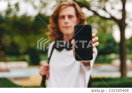 Young person displaying a smartphone in a park setting during the afternoon 132585408