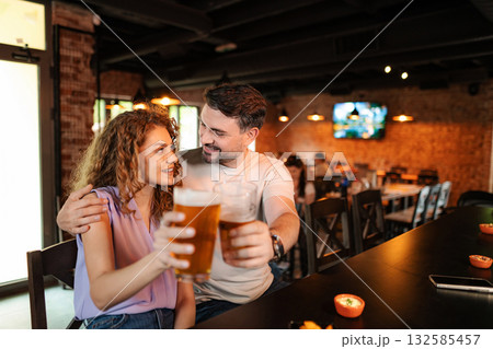 Couple drinking beer and eating snacks at the counter in a pub Couple drinking beer and eating snacks at the counter in a pub 132585457