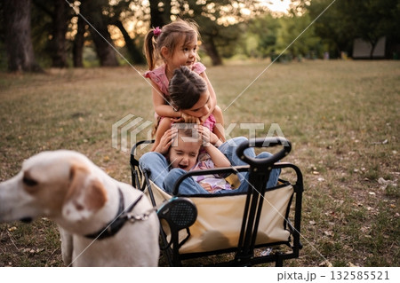 Three sisters are playing in a wagon while their dog watches them 132585521