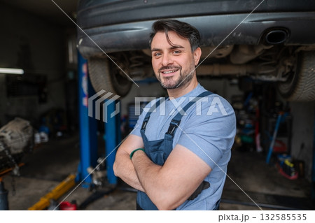 Confident mechanic smiling with arms crossed in his garage 132585535