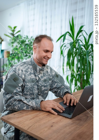 Smiling military man working on laptop at home Smiling military man working on laptop at home 132585539