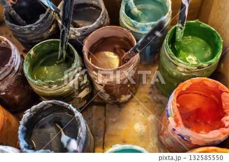 Open jars with multicolored paints in a cardboard box. Open paints in an art workshop. Creative activities 132585550