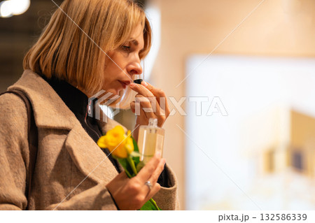 A woman in a beige coat examining a bottle of perfume 132586339