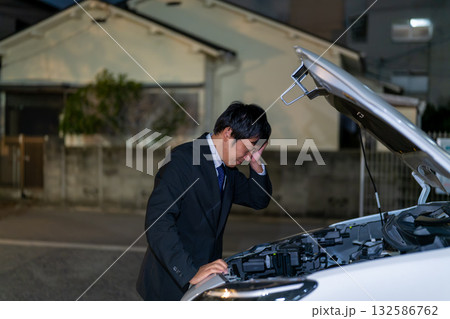夜の路上で車の不具合を確認。車のボンネットを開けてお手上げのスーツの男性。 132586762