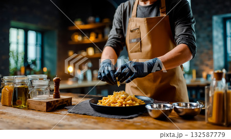 A man in an apron and black gloves preparing pasta in a pan on a wooden table 132587779