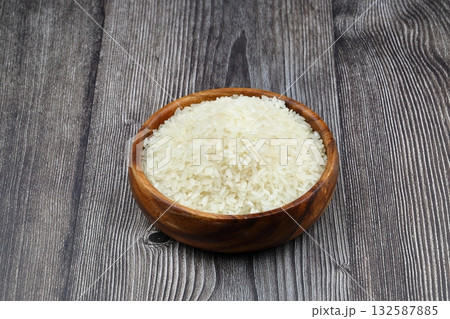 Raw white rice on black background. Long uncooked rice in wooden plate. Natural organic food. Traditional Asian cereal culture. Raw white rice on black background. Long uncooked rice in wooden plate. Natural organic food. Traditional Asian cereal culture. 132587885