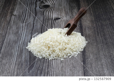 Raw white rice on wooden background. Long uncooked rice in wooden plate. Natural organic food. Traditional Asian cereal culture. Raw white rice on wooden background. Long uncooked rice in wooden plate. Natural organic food. Traditional Asian cereal culture. 132587909