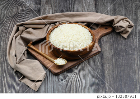 Raw white rice on black background. Long uncooked rice in wooden plate. Natural organic food. Traditional Asian cereal culture. 132587911