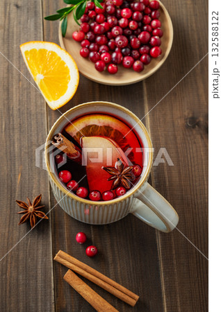 A mulled wine in a mug with cinnamon, berries and fruits on a dark wooden background. A mulled wine in a mug with cinnamon, berries and fruits on a dark wooden background. 132588122