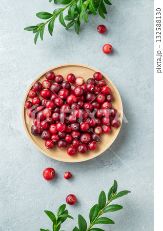 Fresh cranberries in a wooden bowl on a light background with green branch. Fresh cranberries in a wooden bowl on a light background with green branch. 132588130
