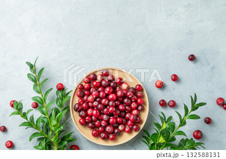 Creative layout of fresh cranberries in a wooden bowl on a light background with green branch. Creative layout of fresh cranberries in a wooden bowl on a light background with green branch. 132588131