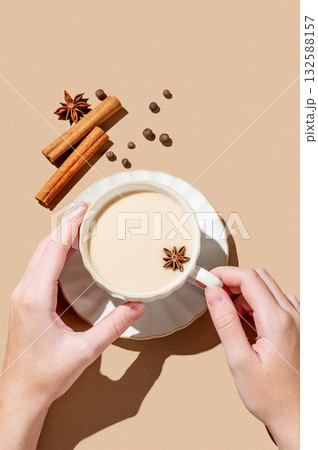 Hand holding cup of traditional Indian masala chai tea with milk and spices on a beige background 132588157