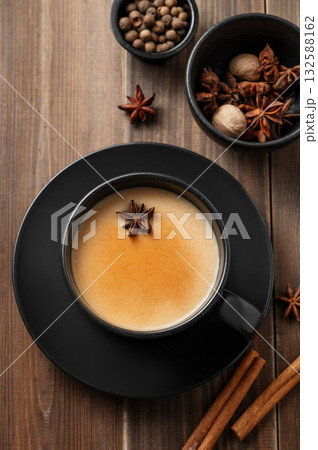 Traditional Indian masala chai tea with milk and spices in a black cup on a dark wooden background 132588162