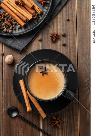 Traditional Indian masala chai tea with milk and spices in a black cup on a dark wooden background 132588164