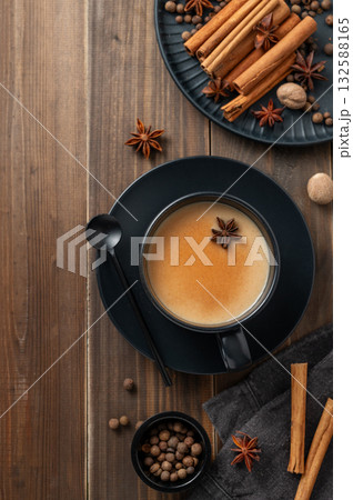Traditional Indian masala chai tea with milk and spices in a black cup on a dark wooden background 132588165
