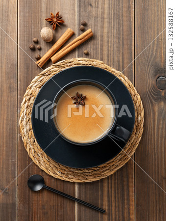Traditional Indian masala chai tea with milk and spices in a black cup on a dark wooden background 132588167