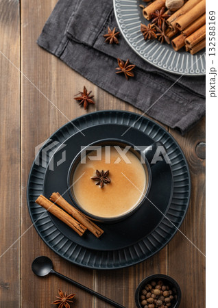 Traditional Indian masala chai tea with milk and spices in a black cup on a dark wooden background 132588169
