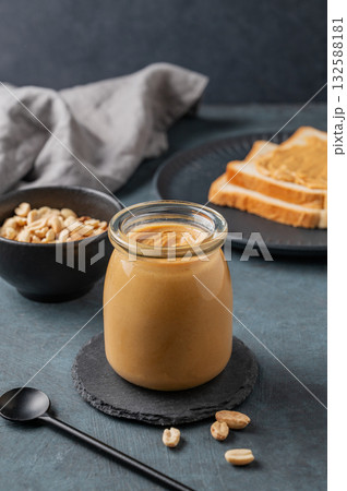 Creamy peanut butter in a jar on a dark background with toasted bread, roasted nuts 132588181