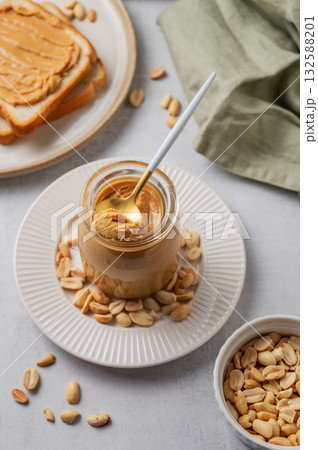 Creamy peanut butter in a jar on a light background with toasted bread, scattered roasted nuts Creamy peanut butter in a jar on a light background with toasted bread, scattered roasted nuts 132588201