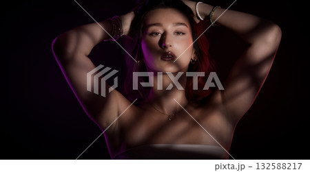 Studio portrait of a young woman posing with colorful lights projected on her Studio portrait of a young woman posing with colorful lights projected on her 132588217