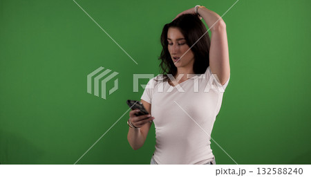 Young woman holding smartphone and posing on green screen background Young woman holding smartphone and posing on green screen background 132588240