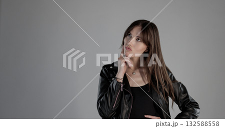 Pensive young woman with leather jacket is thinking and looking up with hand on chin 132588558