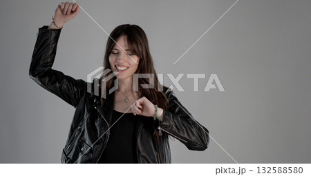 Young woman wearing black leather jacket dancing with eyes closed and gray background 132588580