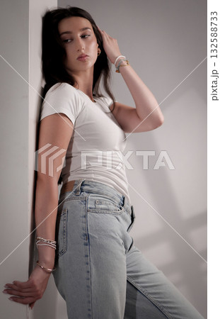 Young woman posing and touching her hair while leaning against a wall 132588733